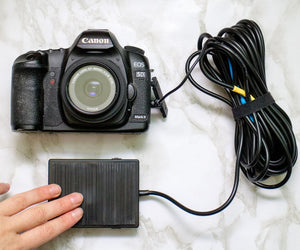 Foot pedal remote shutter release for DSLR camera with long cord connected to a Canon camera